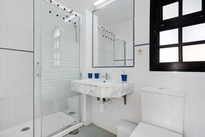 Un bagno con cabina doccia in vetro, un lavandino bianco con piano in marmo e un water bianco.