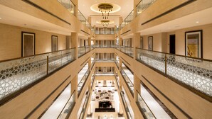 Ein mehrgeschossiges Atrium mit Sitzgelegenheit in der Mitte, Glastrennvorrichtungen und einem modernen Kronleuchter.