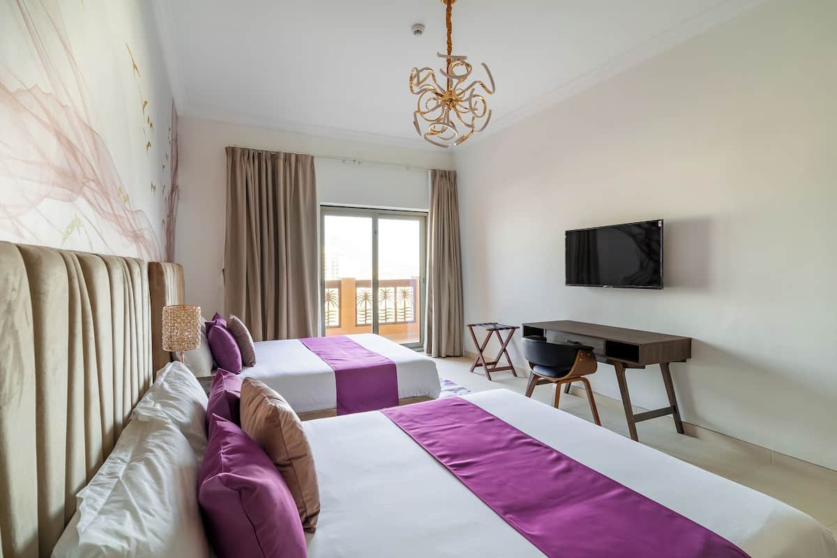 Een hotelkamer met twee bedden, een bureau, een televisie en uitzicht op een balkon.
