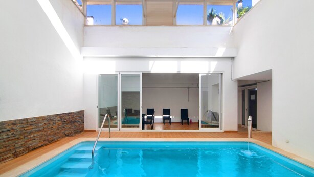 Una piscina interior con cubierta de madera, puertas de cristal que dan a una zona de estar y vistas al cielo a través del techo.
