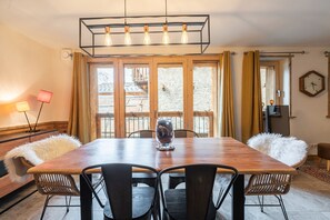 A dining area with a wooden table, black chairs, a decorative glass vase, and a view through large windows.