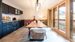 A modern kitchen with dark cabinetry, a wooden dining table, and a view of a snowy landscape through large sliding doors.