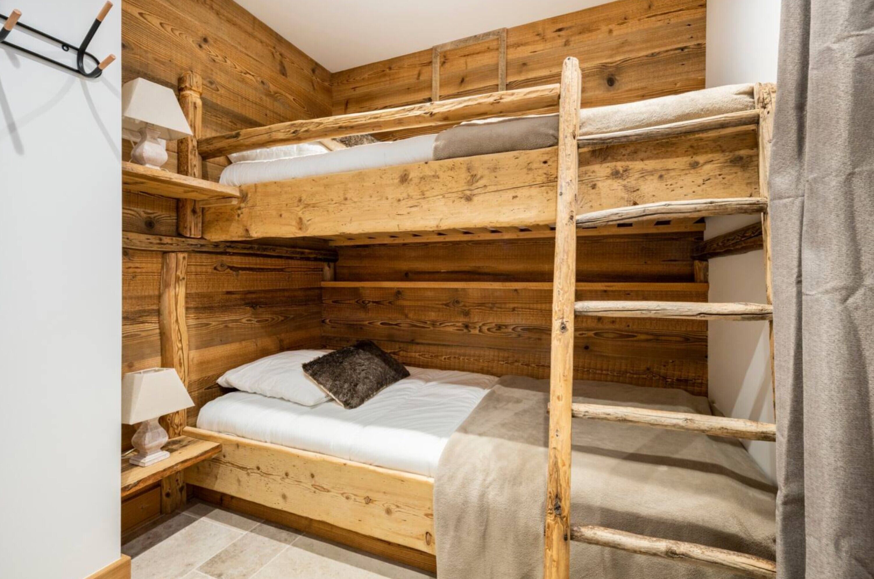A bunk bed room with wooden walls, a bedside table with a lamp, and a grey curtain.