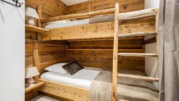 A bunk bed room with wooden walls, a bedside table with a lamp, and a grey curtain.