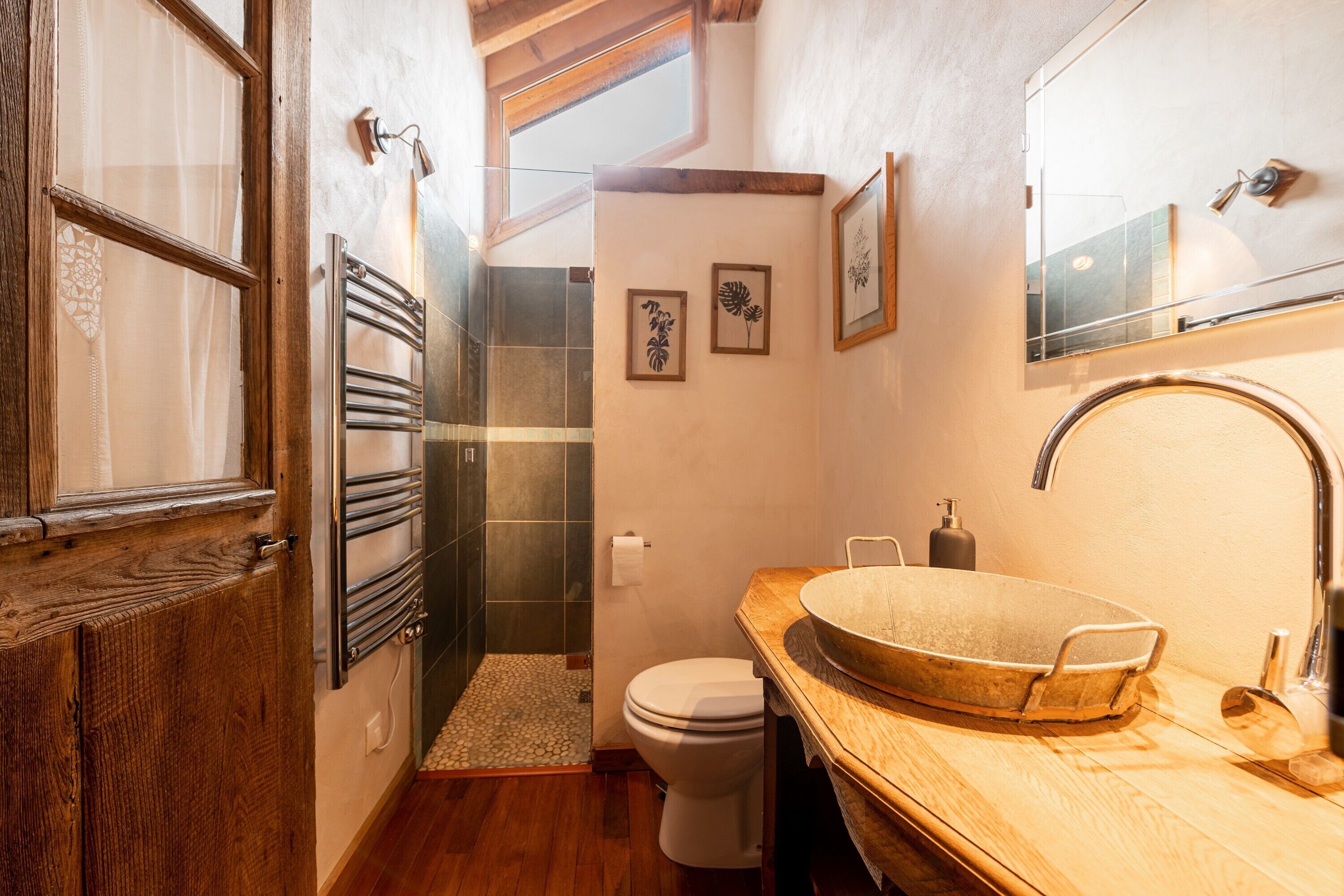 A bathroom with a wooden vanity, a large basin sink, a toilet, a towel rack, and framed artwork on the wall.