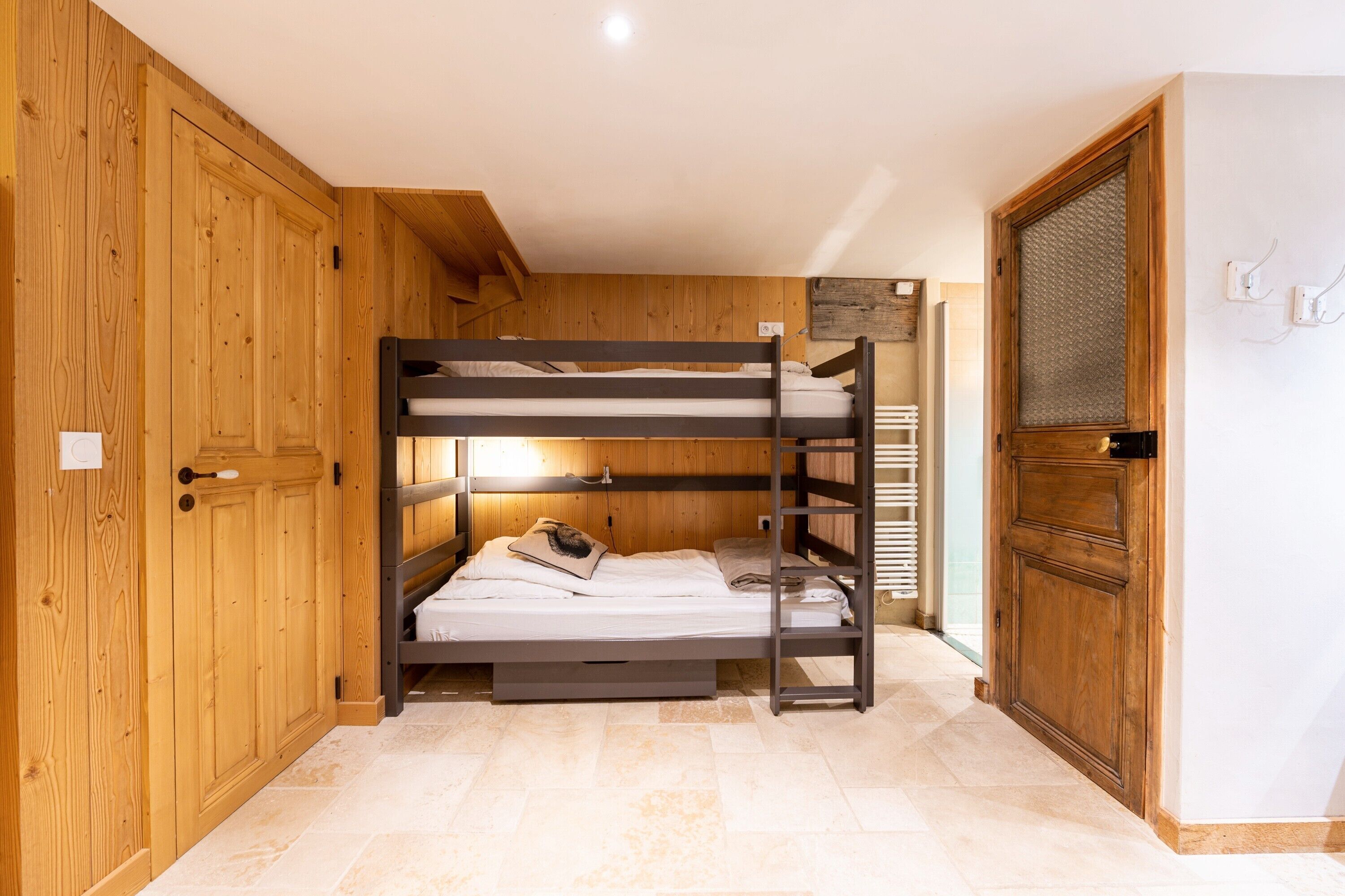 Habitación con literas, paredes de madera, una puerta y suelo de baldosas.
