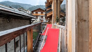 A wooden balcony with a red slide, stone walls, and traditional wooden buildings in the background. - Chalet "Alouette" with Private Terrace, 2 Balconies & Wi-Fi (Champagny-en-Vanoise)