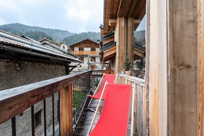 Un balcón de madera con un tobogán rojo, paredes de piedra y edificios de madera tradicionales al fondo.