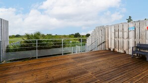 A wooden deck with a metal railing, a bench, and a view of a green landscape.