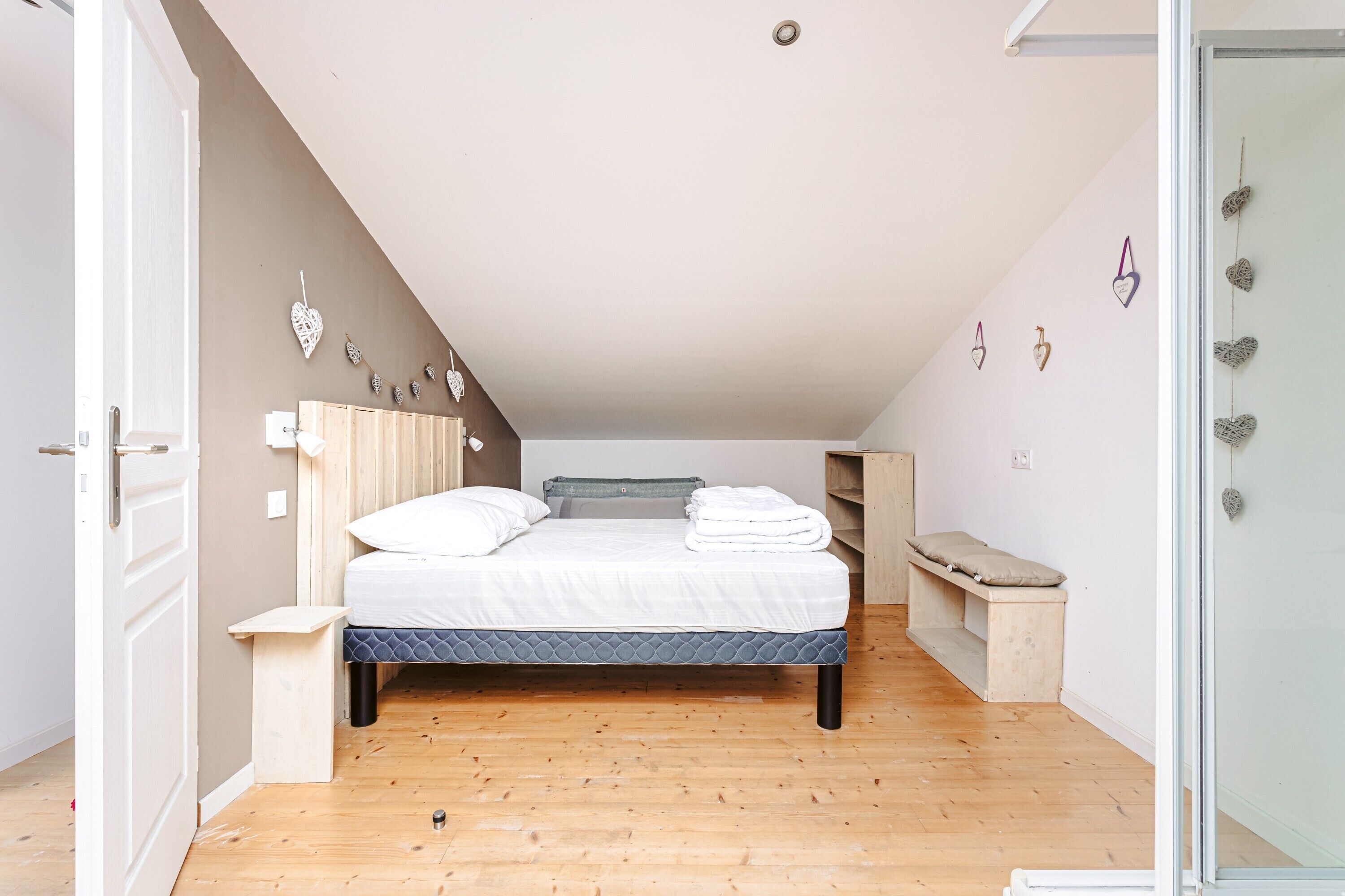 A bedroom with a bed, a bench, a small table, and a wardrobe.
