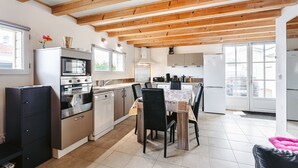 A modern kitchen with wooden beams, stainless steel appliances, and a dining area with a table and chairs.
