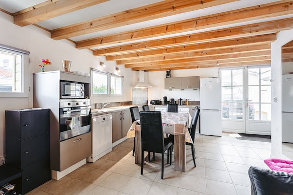 A modern kitchen with wooden beams, stainless steel appliances, and a dining area with a table and chairs.