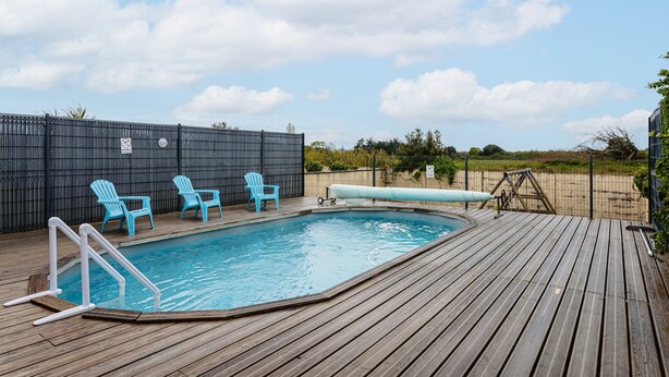 A swimming pool with a wooden deck, three blue chairs, and a slide.