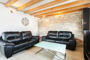 A living room with two black leather sofas, a light-colored coffee table, a brick-patterned wall, and a clock on the wall.