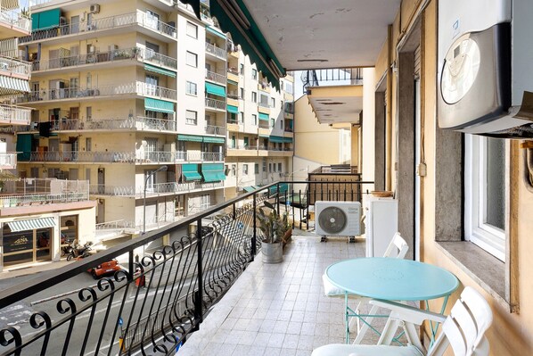 Un balcon avec une table et des chaises, un pot de fleurs et une vue sur des immeubles à plusieurs étages.