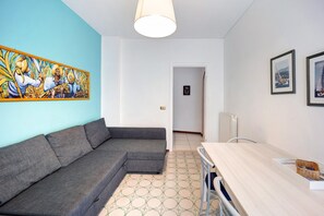 Un salon moderne avec un canapé d’angle gris, une table à manger en bois, un sol à motifs et un grand tableau abstrait accroché au mur.