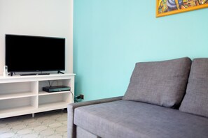 Un salon avec un téléviseur posé sur un meuble blanc, un canapé gris et un mur bleu clair.