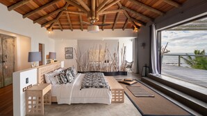 A bedroom with a wooden ceiling, a bed with white bedding, a desk, and a view of the sea. - Koki Bonheur by muse villas (Poste Lafayette)