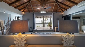 A room with a wooden ceiling, a ceiling fan, a large window with a view of the outdoors, and two lamps on a table. - Koki Bonheur by muse villas (Poste Lafayette)