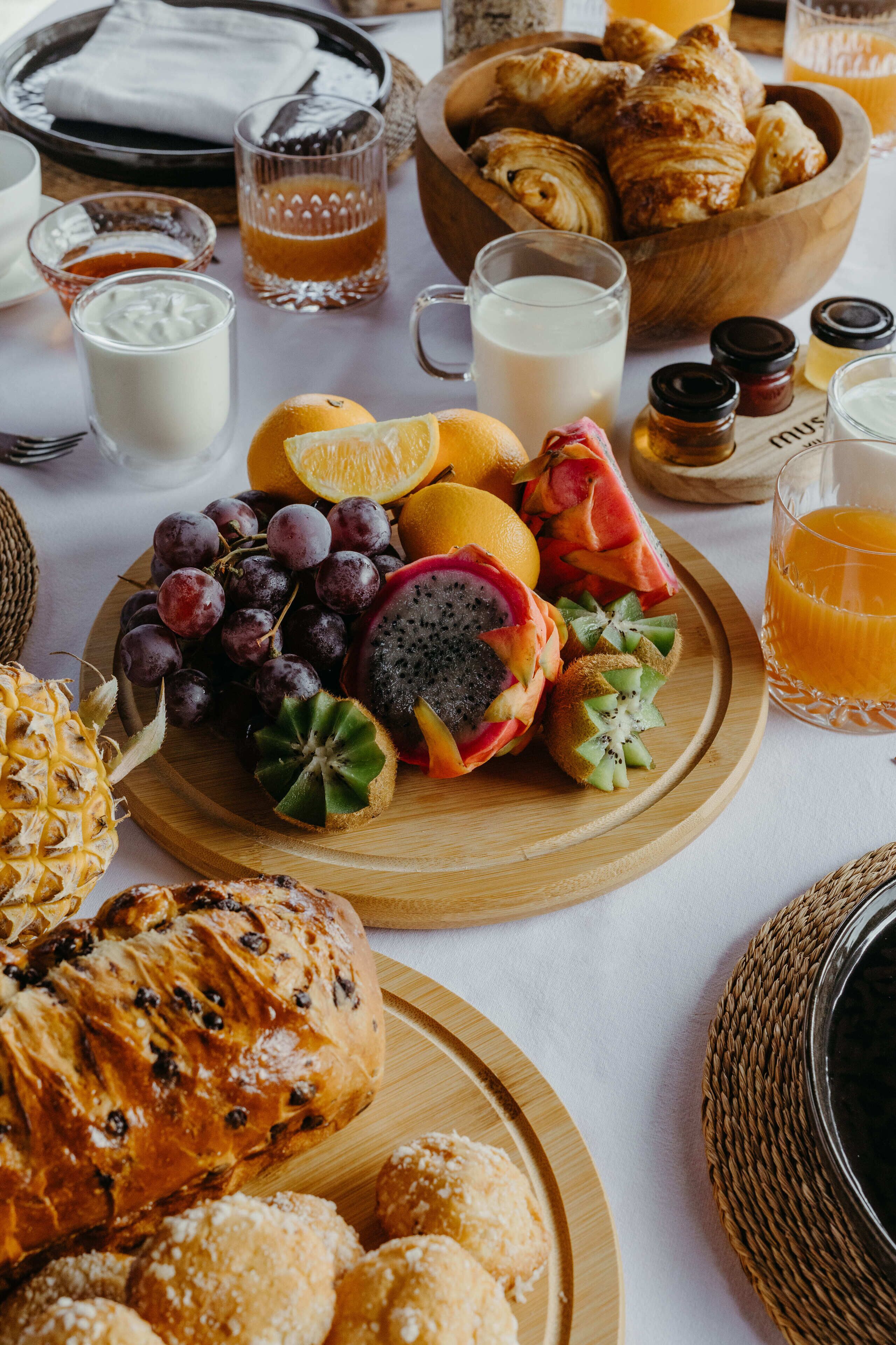 A breakfast setting with a variety of fruits, pastries, and beverages on a table.