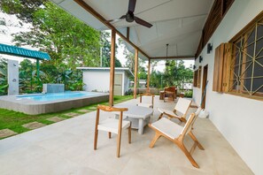Eine überdachte Terrasse mit Pool, Holzstühlen und Deckenventilator.