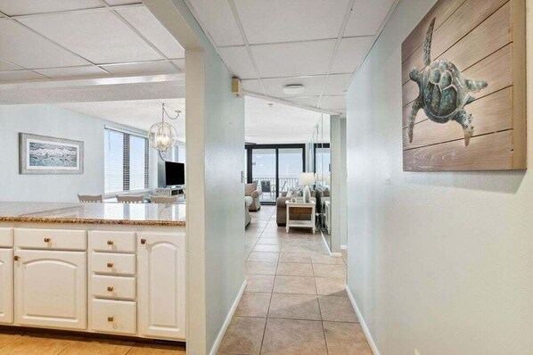 A spacious kitchen with white cabinetry and a large island, a dining area with a view, and a wooden wall with a turtle painting.
