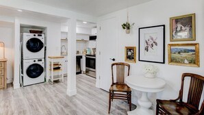 Una cocina moderna con armarios blancos, un comedor con mesa y sillas blancas, y un cuarto de lavado con lavadoras apiladas.