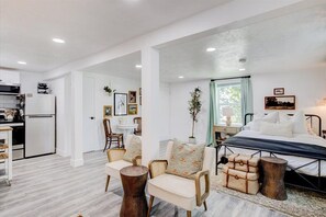 Ein modernes, gut beleuchtetes Zimmer mit Bett, Sitzgelegenheit und Küchenzeile.