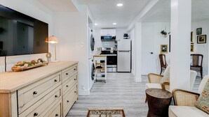 Una cocina moderna con un televisor de pantalla plana, un comedor con una mesa redonda y una sala de estar con un sofá y sillones.
