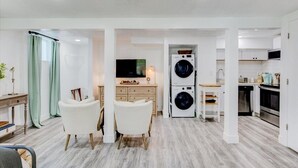 Un espacio habitable compacto con comedor, televisor, lavadora y kitchenette.