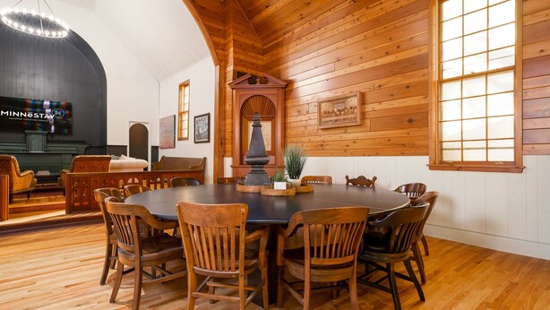 Une salle à manger aux murs lambrés, avec une grande table ronde et des chaises, un lustre et une cheminée.
