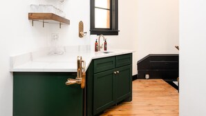 Une cuisine avec un plan de travail blanc, un meuble vert, un plancher en bois et une fenêtre à cadre noir.