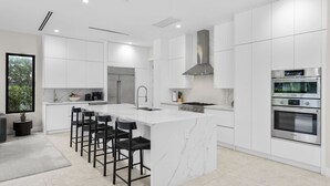 A modern kitchen with white cabinetry, a central island with bar stools, a built-in oven, and a large window.