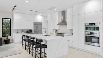 Une cuisine moderne avec des meubles blancs, un îlot central doté de tabourets, un four encastré et une grande fenêtre.