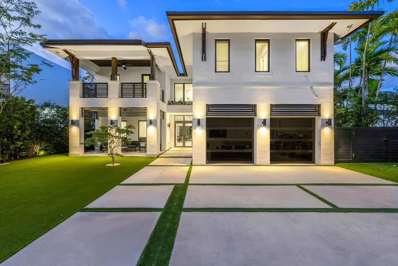 Une maison moderne à deux étages, dotée d’un patio couvert, d’un garage et d’une pelouse bien entretenue.