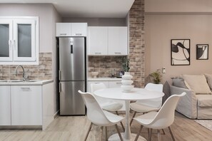 Une cuisine moderne avec des meubles blancs, un réfrigérateur en acier inoxydable et un coin repas comprenant des chaises blanches et une table ronde.