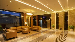 A modern lobby with a large sectional sofa, a chandelier, and a reception desk. - V FIVE HOTEL (Chengalpattu)