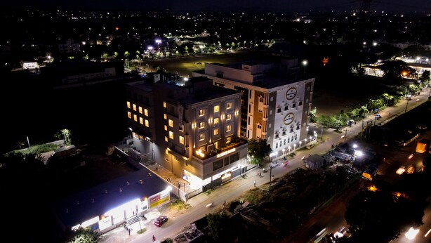 A multi-story hotel with illuminated windows and a prominent sign on the ground floor. - V FIVE HOTEL (Chengalpattu)