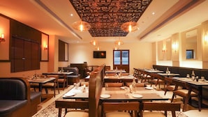 A restaurant with wooden booths and tables, a patterned ceiling, and wall-mounted lights. - V FIVE HOTEL (Chengalpattu)
