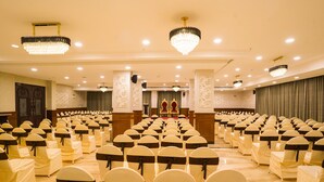 A banquet hall with rows of chairs, a stage with a red carpet, and chandeliers. - V FIVE HOTEL (Chengalpattu)