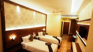 A hotel room with two beds, a TV, a desk, and a bathroom visible in the background. - V FIVE HOTEL (Chengalpattu)