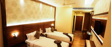 A hotel room with two beds, a TV, a desk, and a bathroom visible in the background.