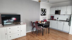 Eine moderne Küche mit weißen Schränken, einem Essbereich mit Tisch und Stühlen sowie einem Fernseher auf einem weißen Korpus.