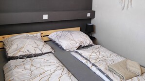 Ein Schlafzimmer mit einem Bett, das ein Baumast-Muster zeigt, einem Wand-Dreamcatcher und einem Gemälde mit Waldszene über dem Bett.