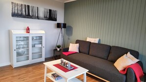 Ein Wohnzimmer mit einem dunkelgrauen Sofa, weißen Kissen, einer roten Decke, einem weißen Couchtisch und einem Schrank mit Glastüren.