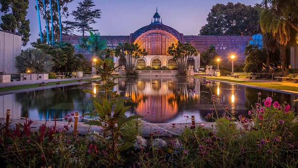 A tranquil garden with a reflective pond, a gazebo, and a building with a dome.