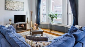 A living room with a large blue sofa, a coffee table, a TV, and a window with curtains.