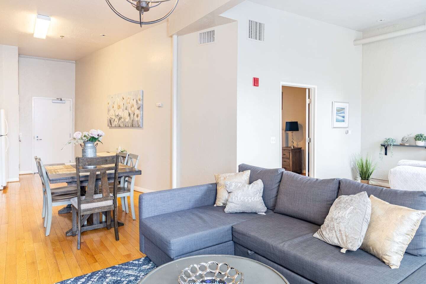 A modern living room with a grey sectional sofa, a dining table with chairs, and a small coffee table.