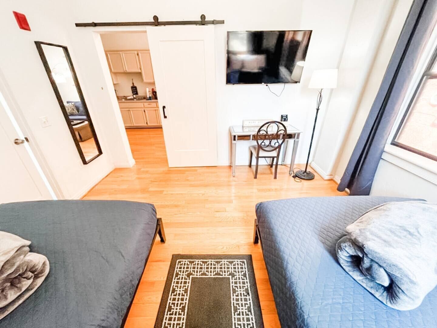 A bedroom with two beds, a desk with a chair, a TV, and a window.