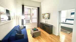 Un salon avec un canapé bleu, un téléviseur fixé au mur et une fenêtre avec des rideaux.